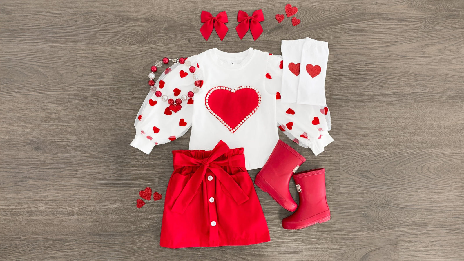 A charming red skirt set and matching onesie featuring delicate heart and pearl accents, perfect for your little love bug. Made from soft and cozy fabric, this outfit ensures comfort during all adventures. Ideal for Valentine's Day, it pairs beautifully with Sparkle in Pink (SIP) bows and booties, creating an irresistibly adorable look.